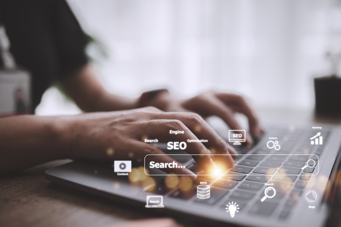 Mãos digitando em notebook com ícones digitais e termo SEO, ilustrando estratégia de SEO semântico e otimização de conteúdo. 